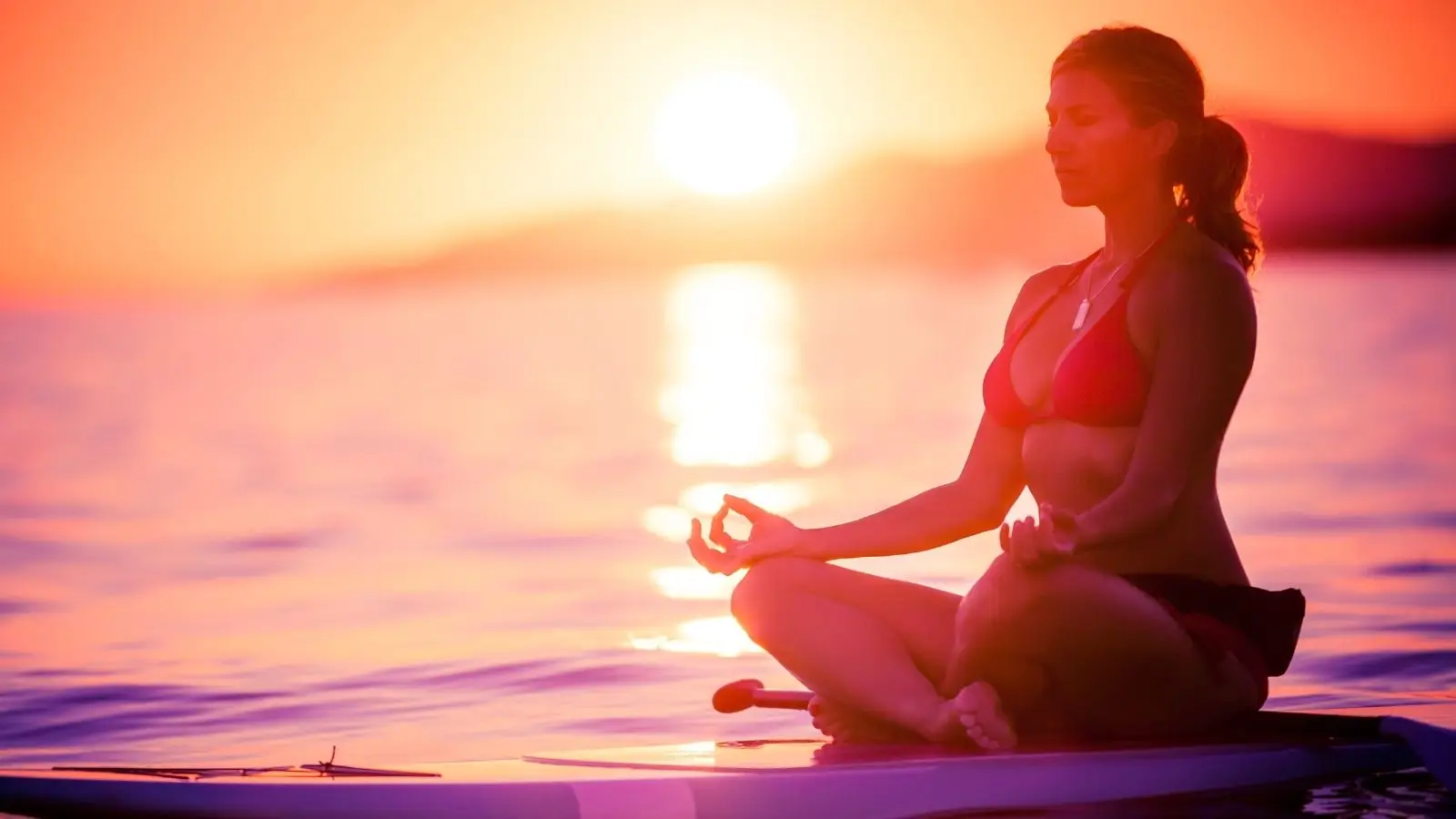 Woman meditating on paddleboard at sunset